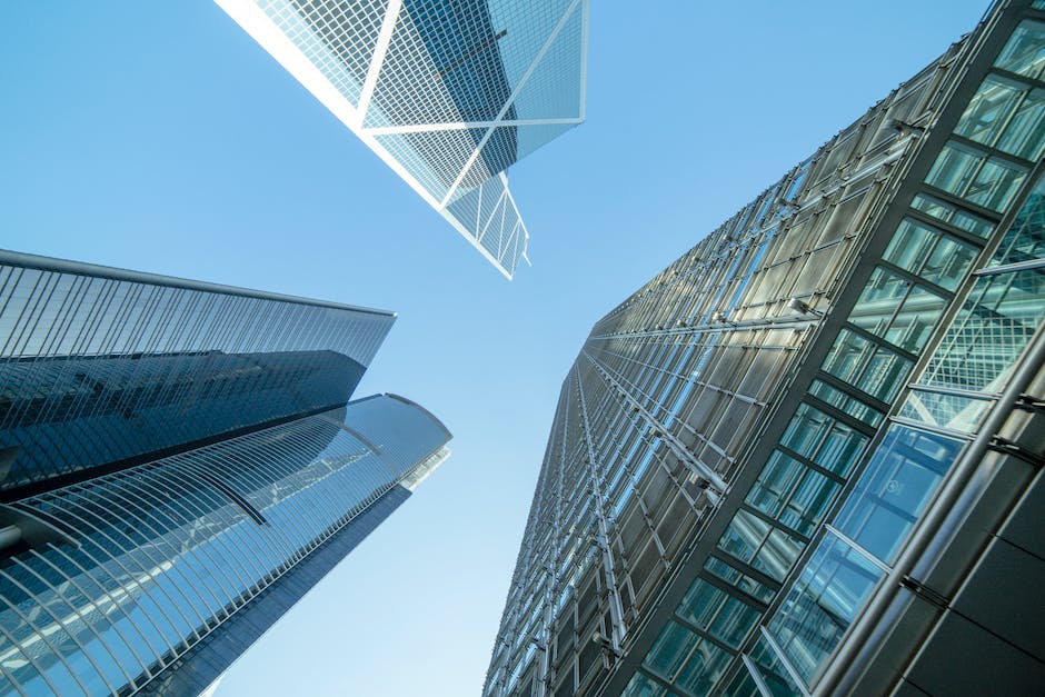 A low-angle upward view of modern glass and steel skyscrapers against a clear blue sky, showcasing contemporary urban architecture and geometric design.