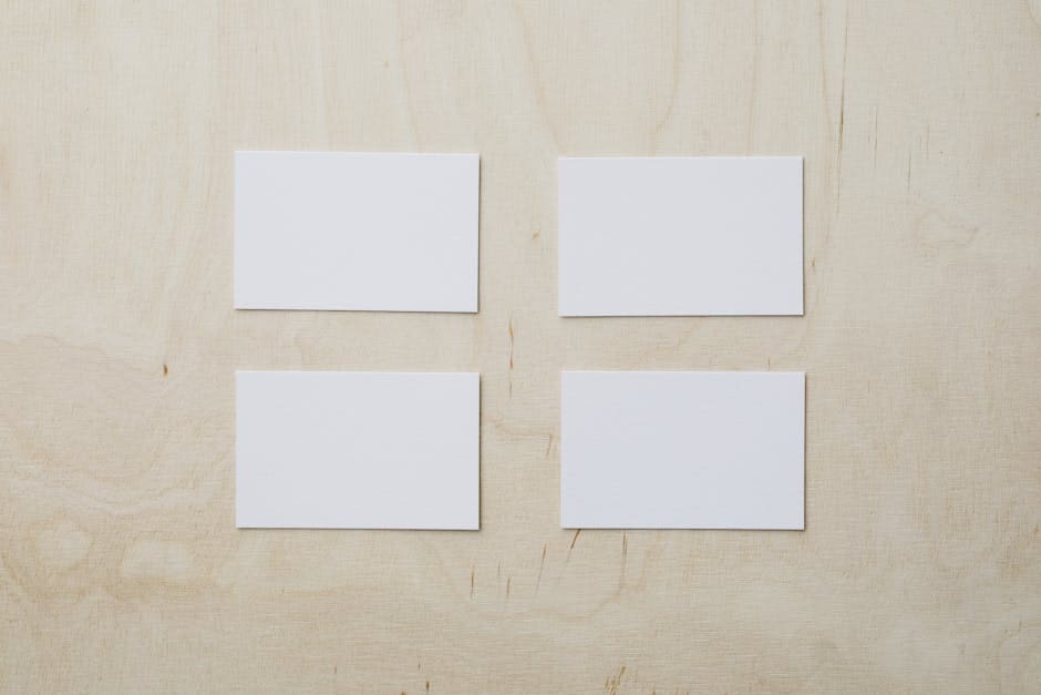 Four blank white rectangular cards or papers arranged in a grid pattern on a light textured wall surface.