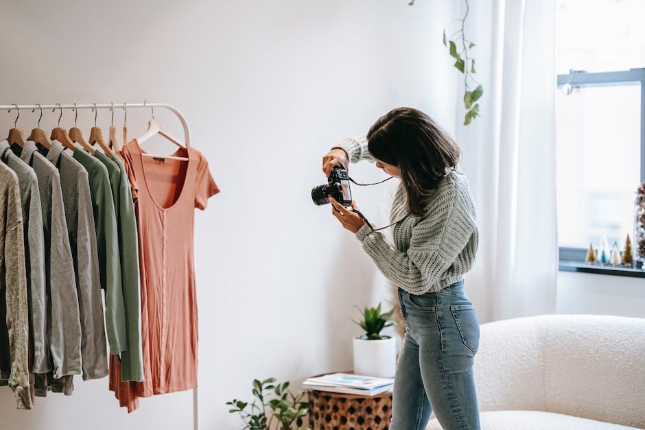 A fashion photographer captures clothing on a rack in a bright, minimalist interior studio space with natural window light.