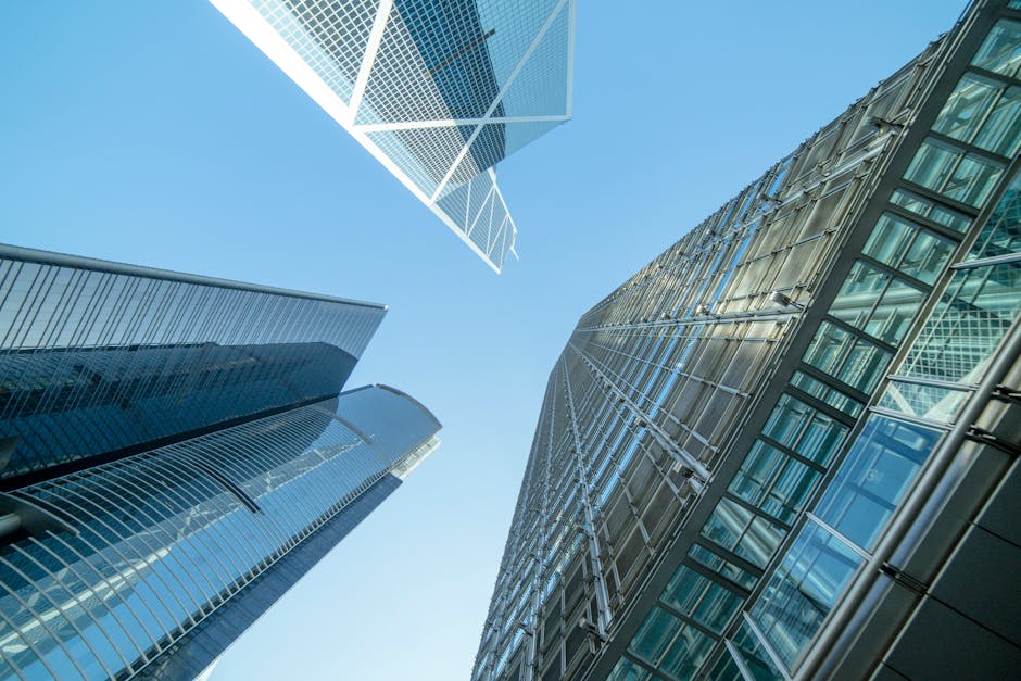 A low-angle upward view of contemporary glass and steel skyscrapers against a clear blue sky, showcasing modern urban architecture.