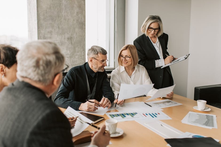 A group of business professionals gathered around a conference table reviewing documents during a formal meeting or workshop session.